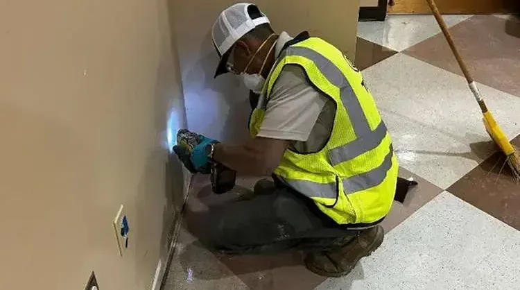 Technician in a safety vest checking a wet wall with a moisture meter in a home