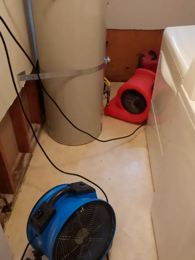 Air movers drying a laundry area with the wall opened behind the washer, an appliance leak dry-out