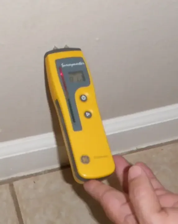Pin moisture meter reading a baseboard during a water damage check