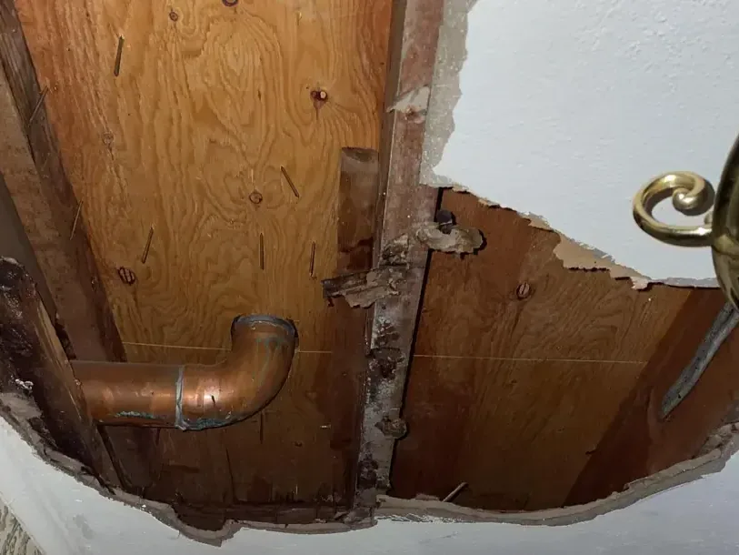 Ceiling opening exposing a copper drain pipe and wood framing