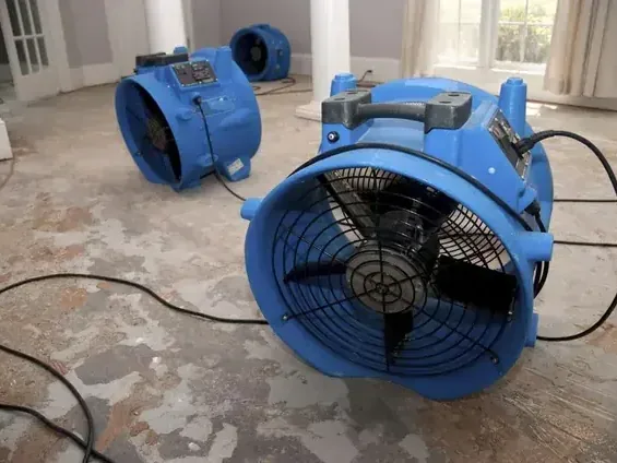 Two blue air movers on a stripped interior floor near bright windows
