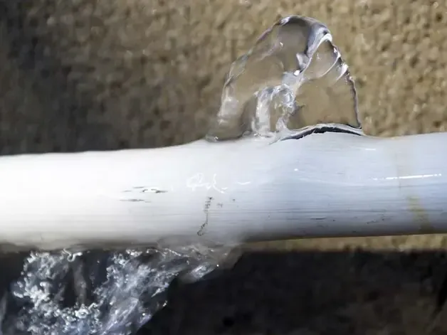 Water spraying from a split white pipe against a rough textured background