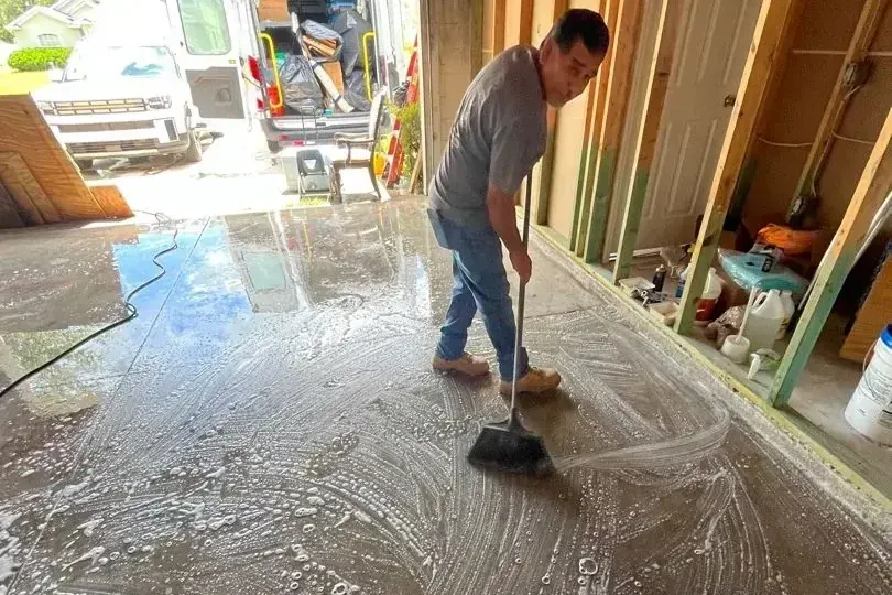 A man sweeping water across a stripped floor toward an open doorway