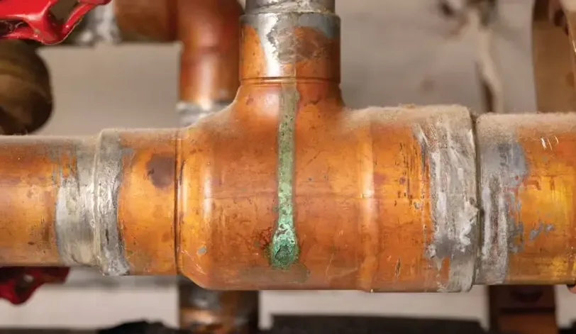 Green corrosion mark below a pinhole leak in a copper pipe fitting