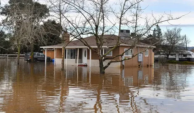 Floodwater surrounding a single-story home and nearby trees