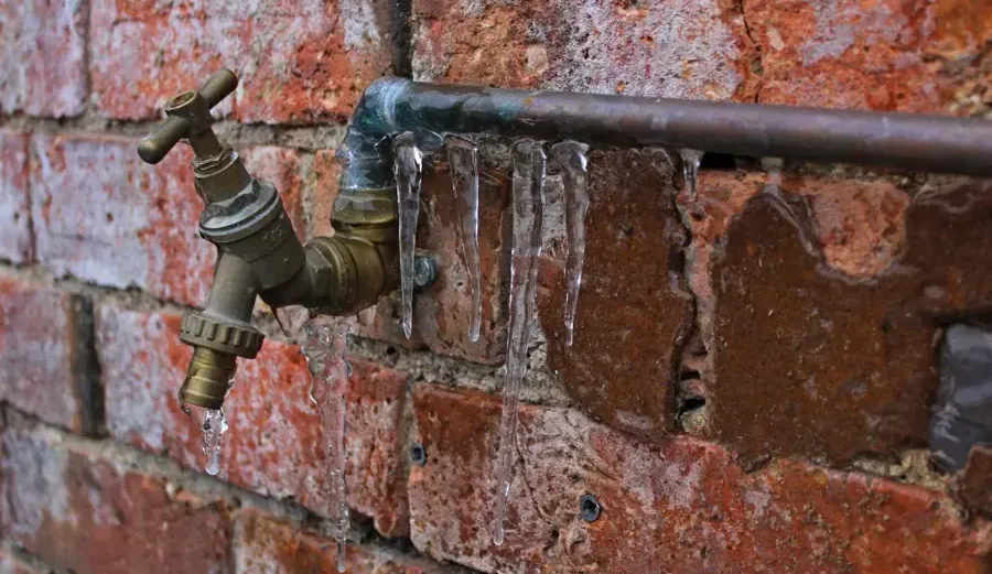 Ice hanging from an outdoor water spigot and pipe on a brick wall